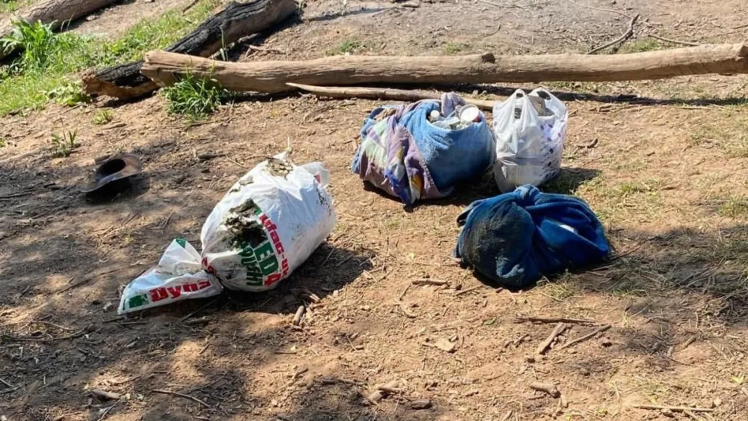 Four piles of bagged rubbish and dirty towels are on the ground in the dirt.