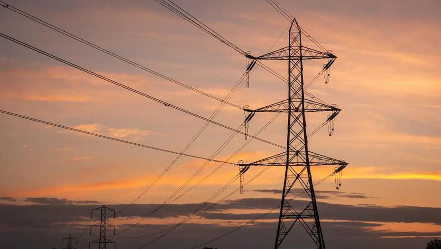 A dark electricity pylon with wires attached. There is a sky with an amber glow in the background.