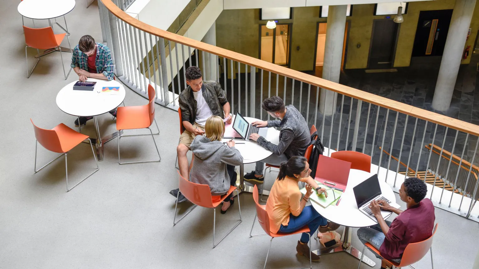  Students sit on three tables. they sit at their laptops doing work. the pictures it taken from a high angle.