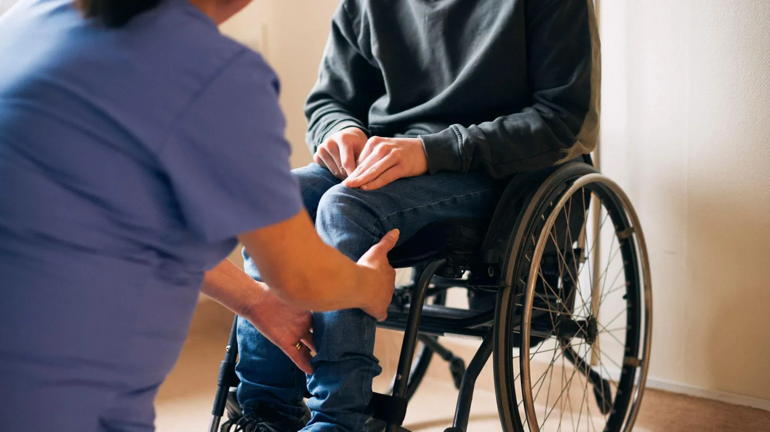 Midsection of female healthcare expert examining leg of patient sitting on wheelchair in medical clinic