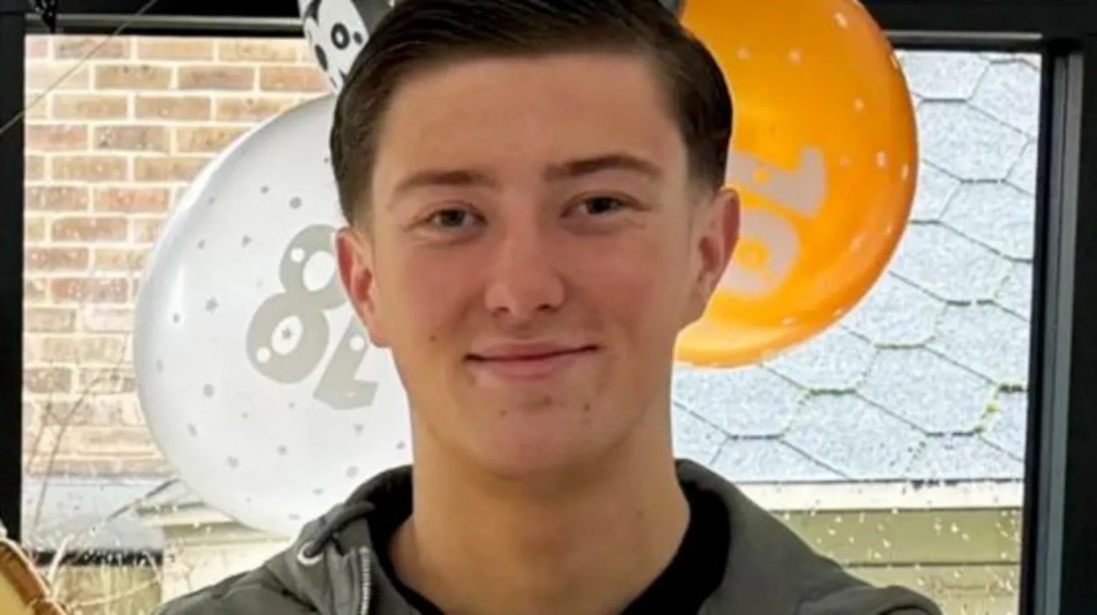 Police handout An 18-year-old man standing in front of orange, white and black balloons by a window. He has short dark hair and is smiling and is wearing a blue jacket and a black top underneath.