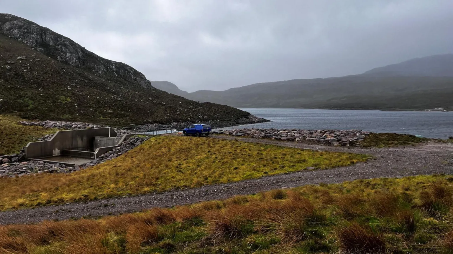 A Highland loch with a dam to the left and a blue pickup truck.