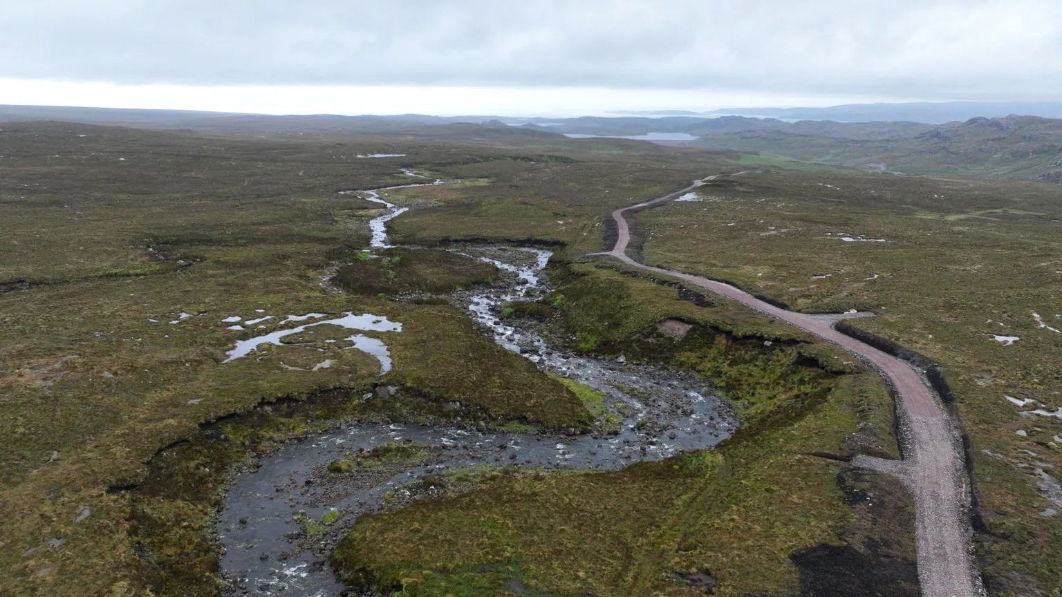 A Highland landscape with a river running into the distance alongside a relatively new looking vehicle track.
