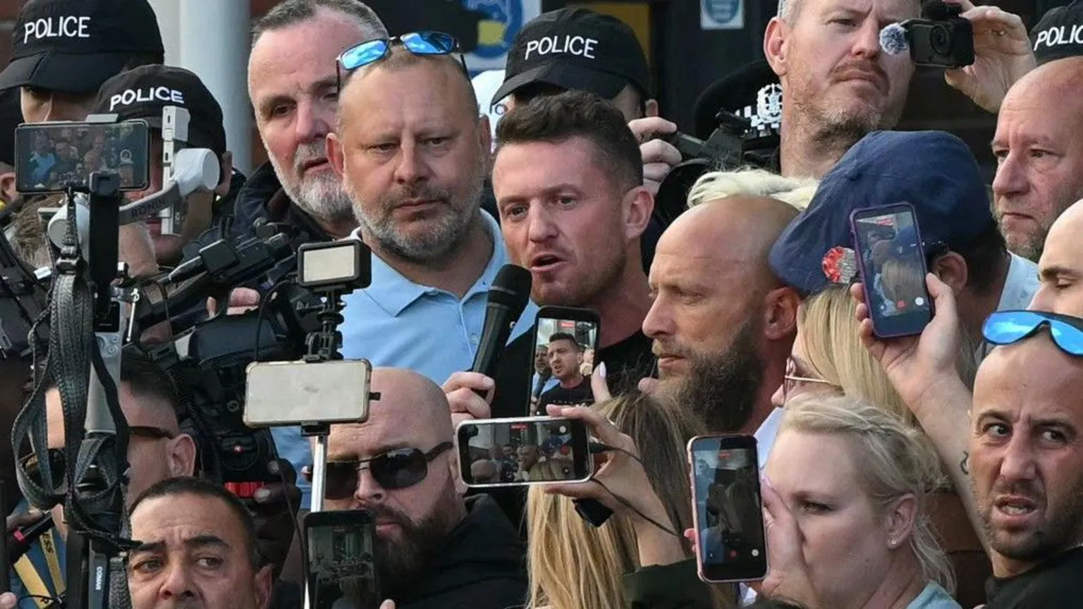  Tommy Robinson is pictured speaking to a microphone while surrounded by a large group of people. 
