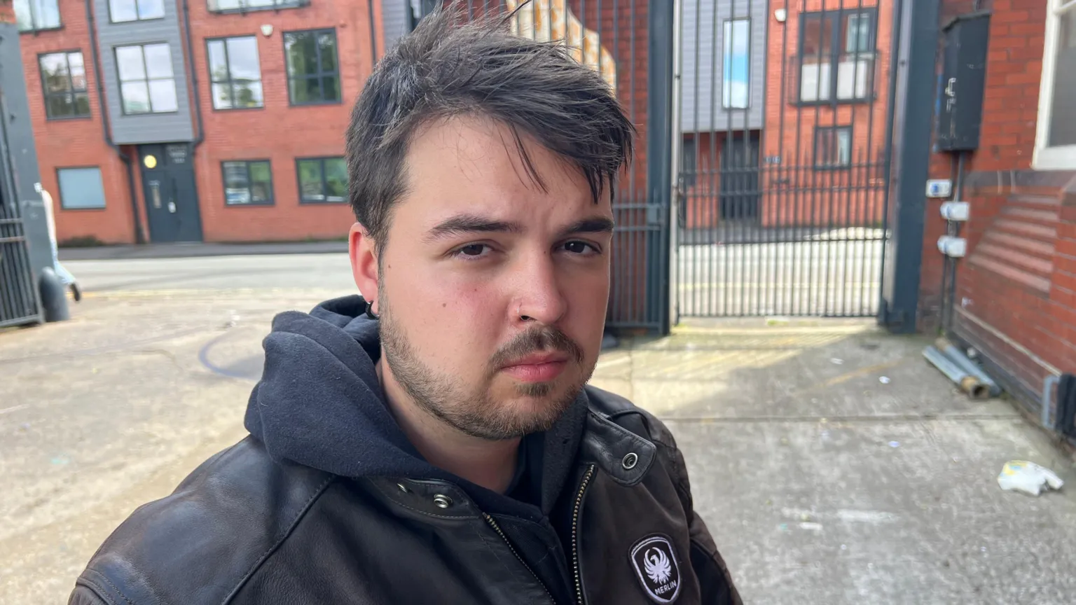 Lewis Jeffries. He has short dark hair and facial hair. He is pictured wearing a black hoodie and black leather jacket. 
