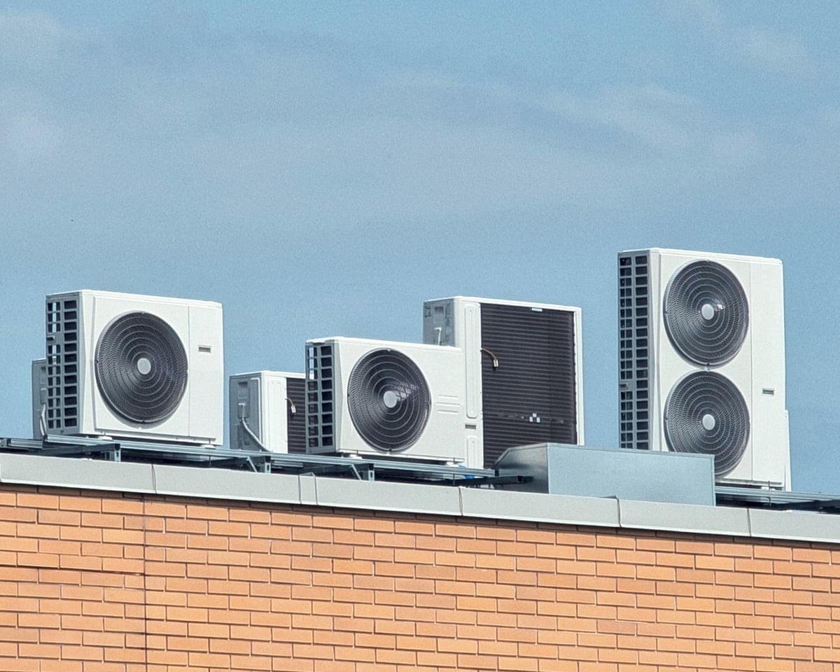 Rooftop air conditioning units for building climate control against a blue skySeveral white air conditioning condenser units are installed on the flat roof of a building. The units vary slightly in size and are set against a clear blue sky with a few wispy clouds.