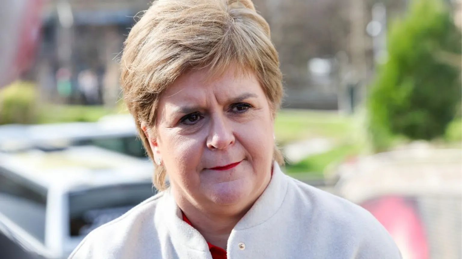 Nicola Sturgeon, who has short fair hair, in a close-up shot. She is wearing a white jacket and standing outside on a sunny day.