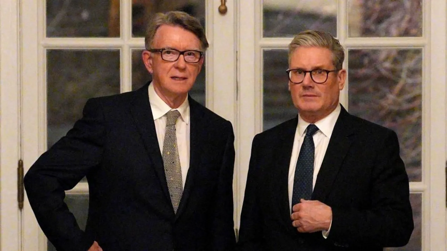 Carl Court/PA Lord Mandelson and Sir Keir Starmer are stood in front of two white framed, glass-panelled doors. They are staring straight ahead and both wearing dark coloured suits, white shirts and patterned ties.