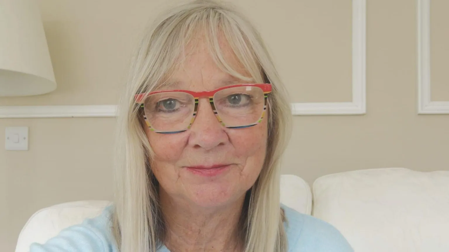 Joyce Craig A woman with blonde hair and wearing a blue jumper. She is wearing red and blue glasses.