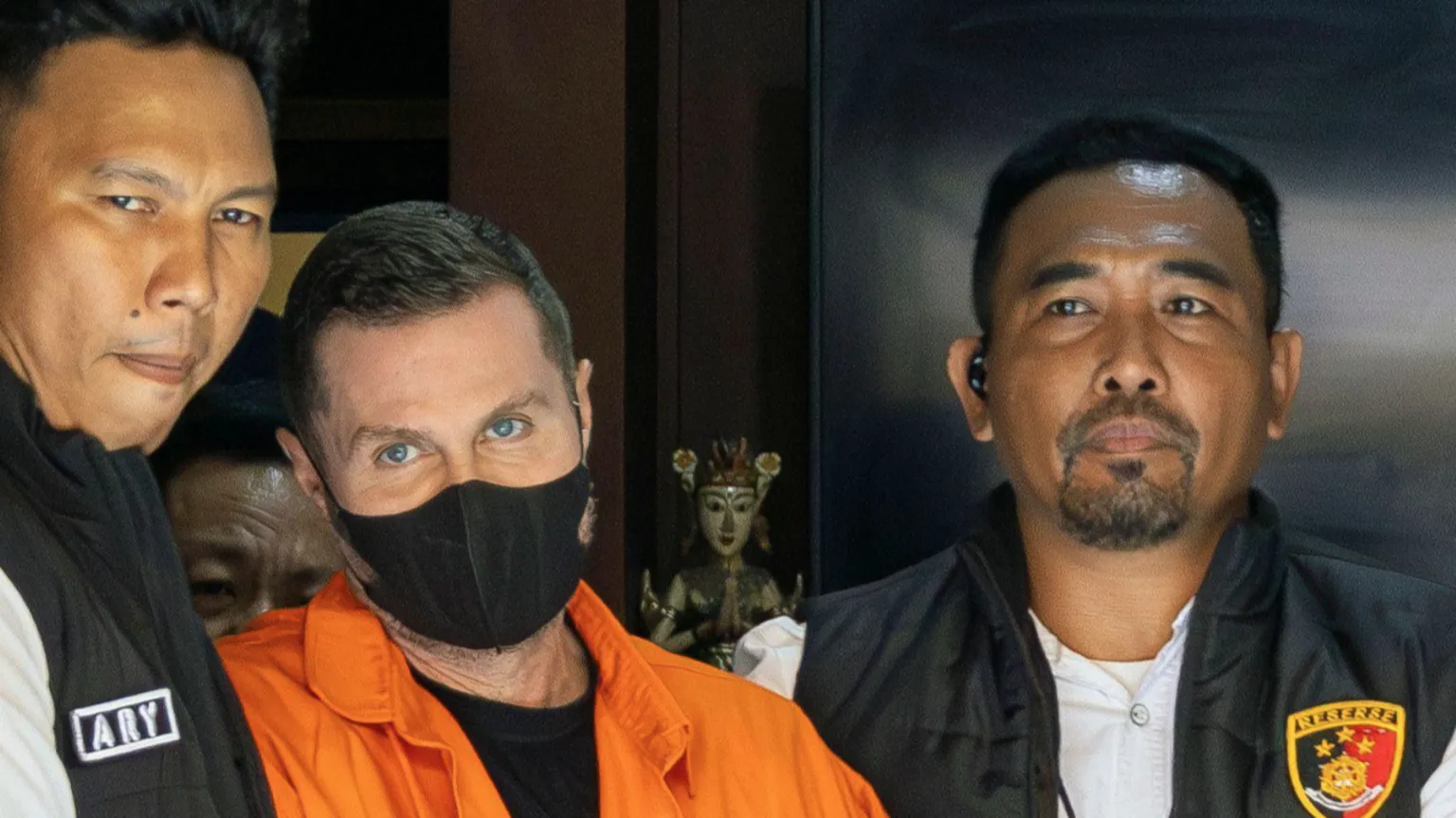 EPA Steven Lyons, wearing a black face mask and an orange boiler suit, is flanked by police officers