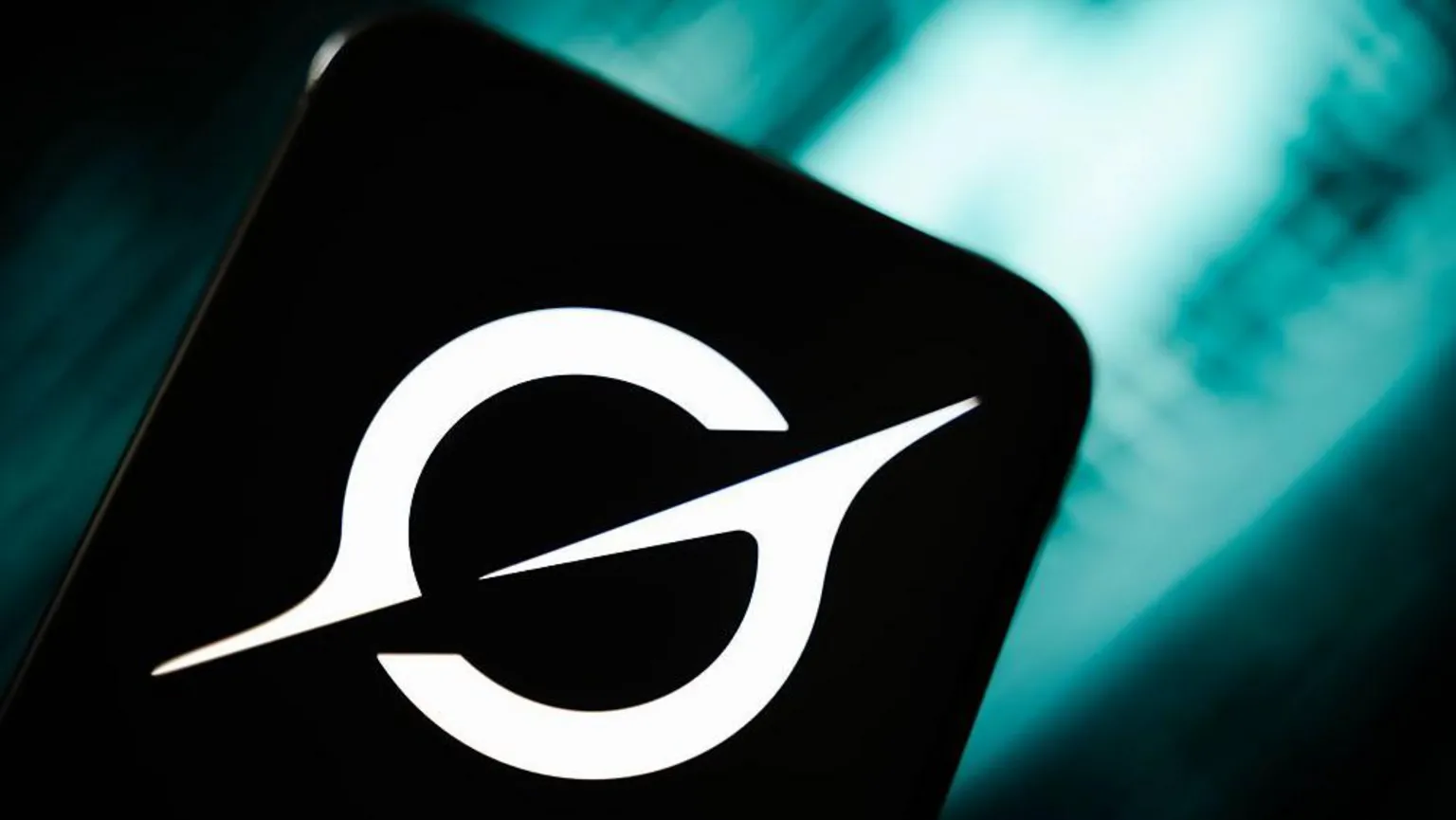 An image of the white Grok logo on a smartphone in front of a teal coloured blurred abstract background.