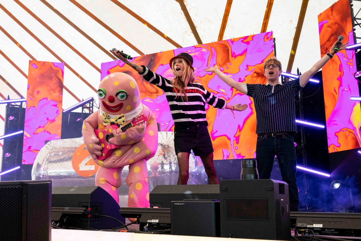 An inflatable pink creature with yellow spots on stage with two musicians