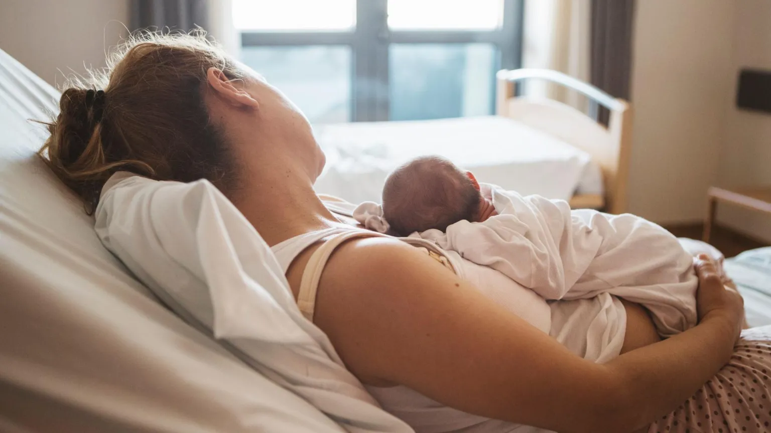  Mother lying down on a hospital bed with her newborn baby on her chest 