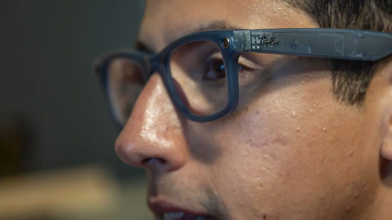 Close-up profile of a person wearing translucent, dark grey Ray-Ban smart glasses featuring a small built-in camera lens near the hinge.