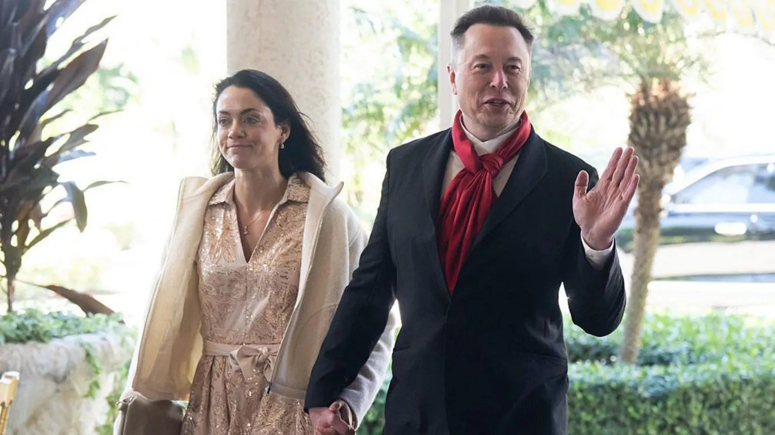 AFP via Shivon Zillis, wearing a pink metallic dress and cream jacket, walks hand in hand with Musk, who wears a red scarf, white shirt and black suit, as he waves to photographers.