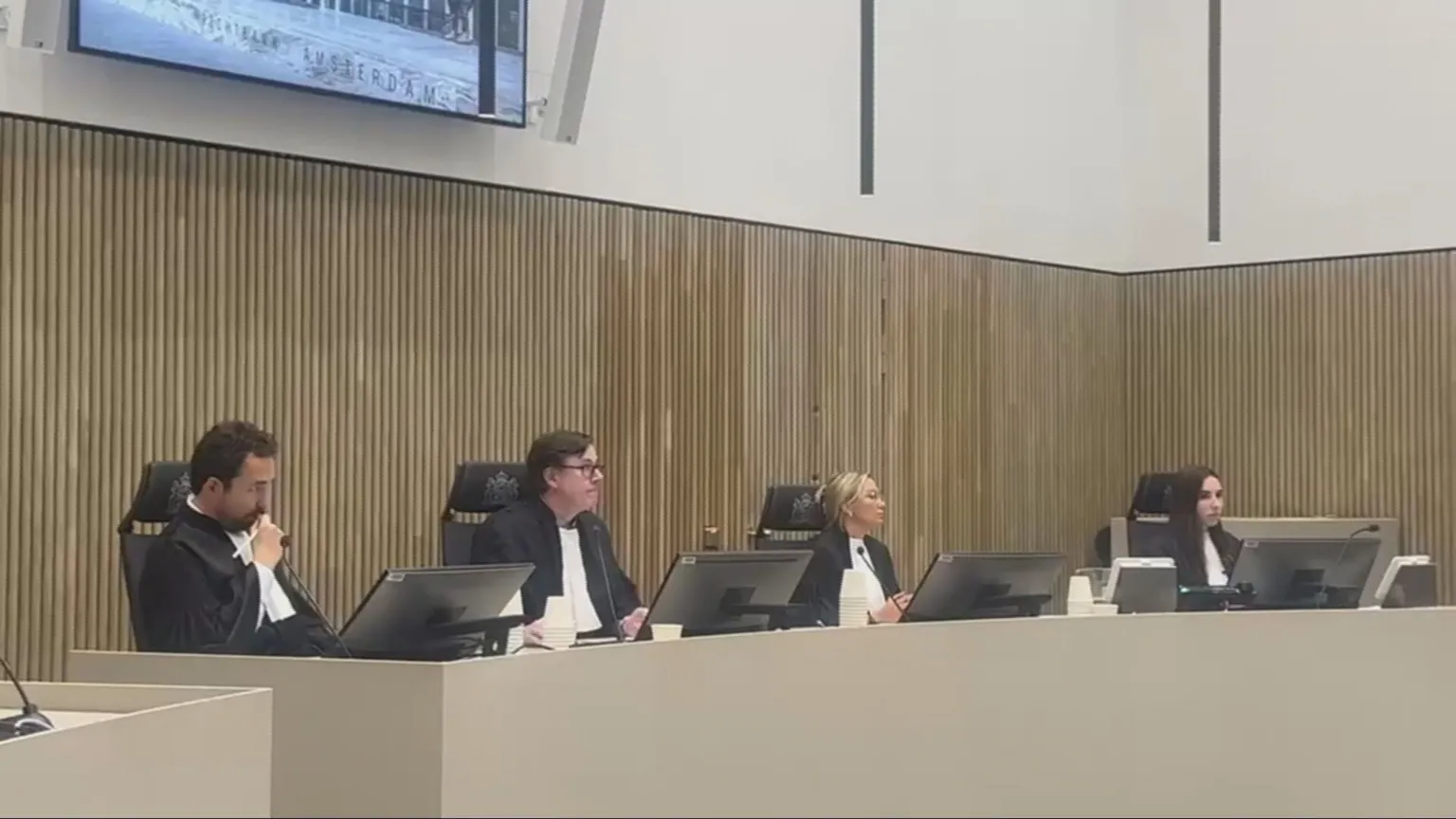 A courtroom with three judges sitting, plus a furth person taking information down.