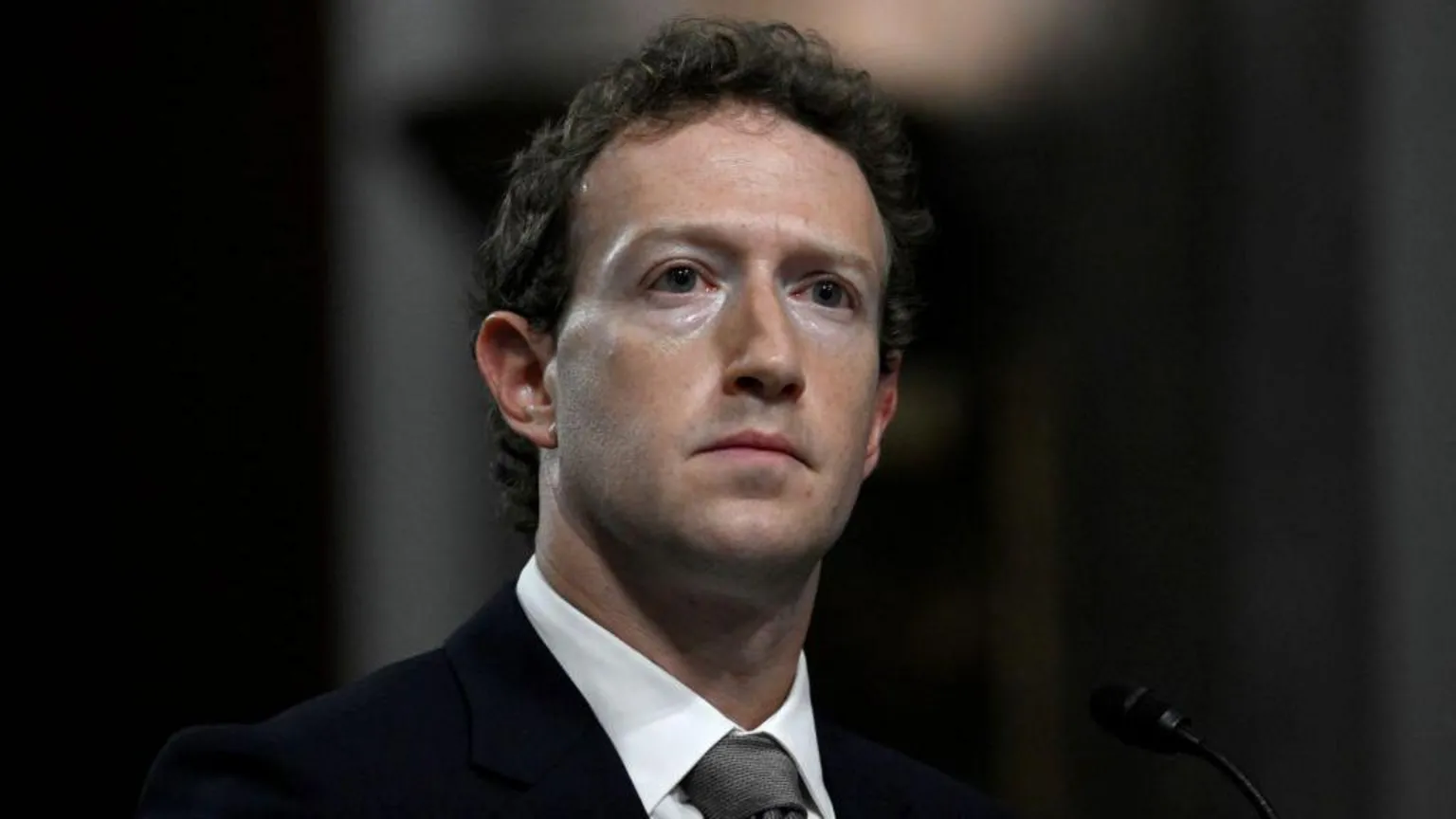 AFP via Mark Zuckerberg, wearing a suit and grey tie, looks away from the camera with a grave expression as he is questioned by US lawmakers during a 2024 Senate hearing