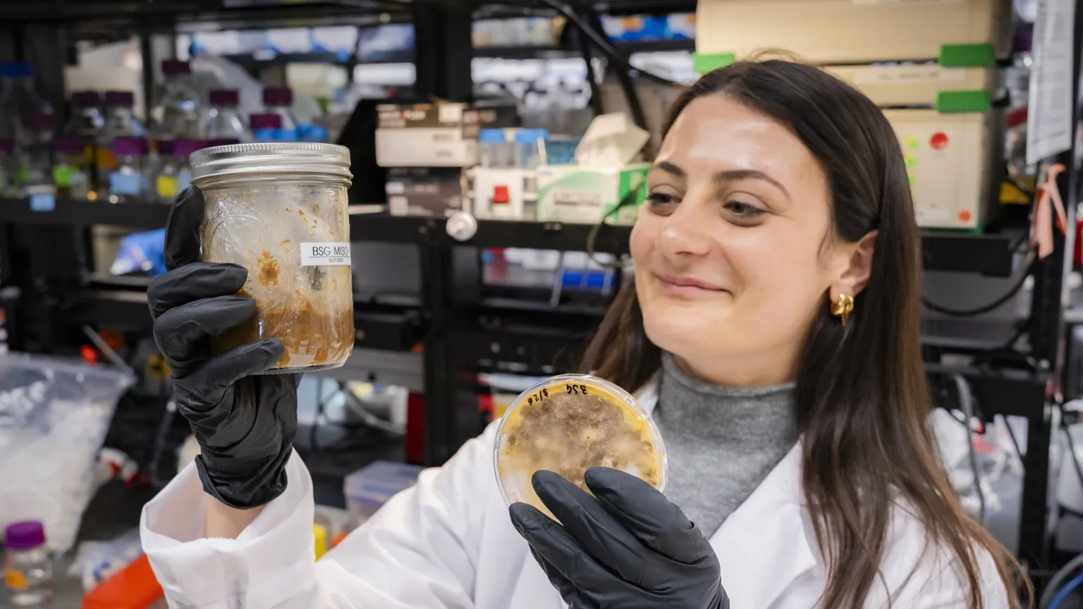 Franklin Lurie A female researchers wearing a lab coat holds up a jar and a petridish containing fungi.