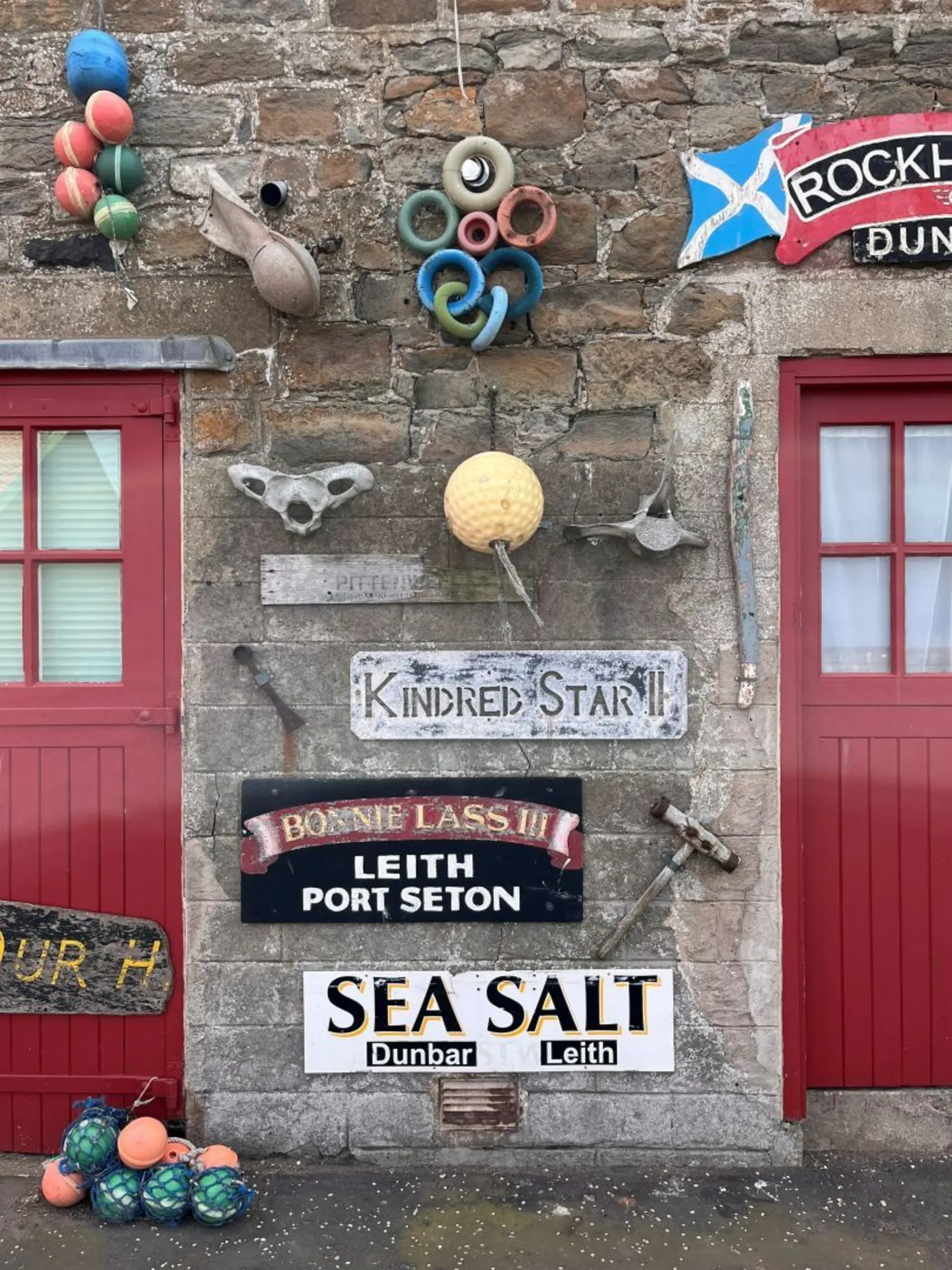 Hugh Kerr A stone wall with two red doors decorated with different signs and fishing paraphernalia. 