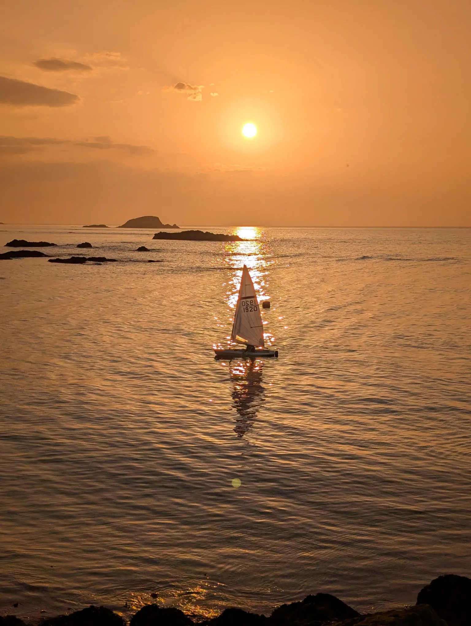 John Welsh An orange sunset over the water. A boat sails below the sun.