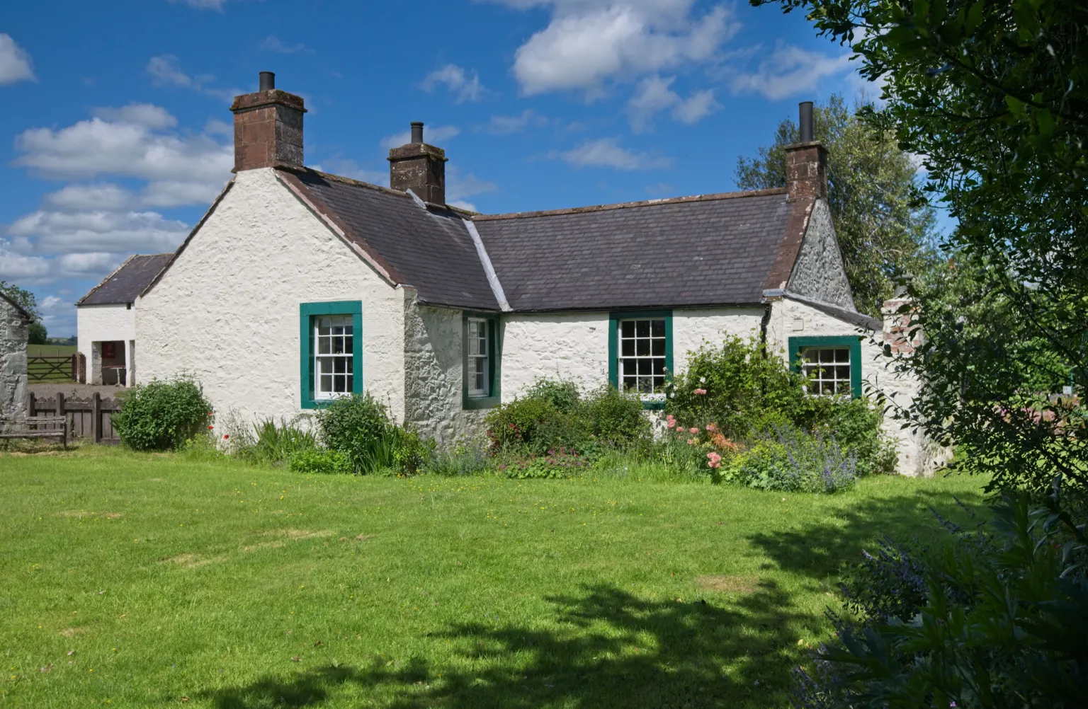 Ian Findlay White farm buildings with green window frames. Trees and bushes surround the property.
