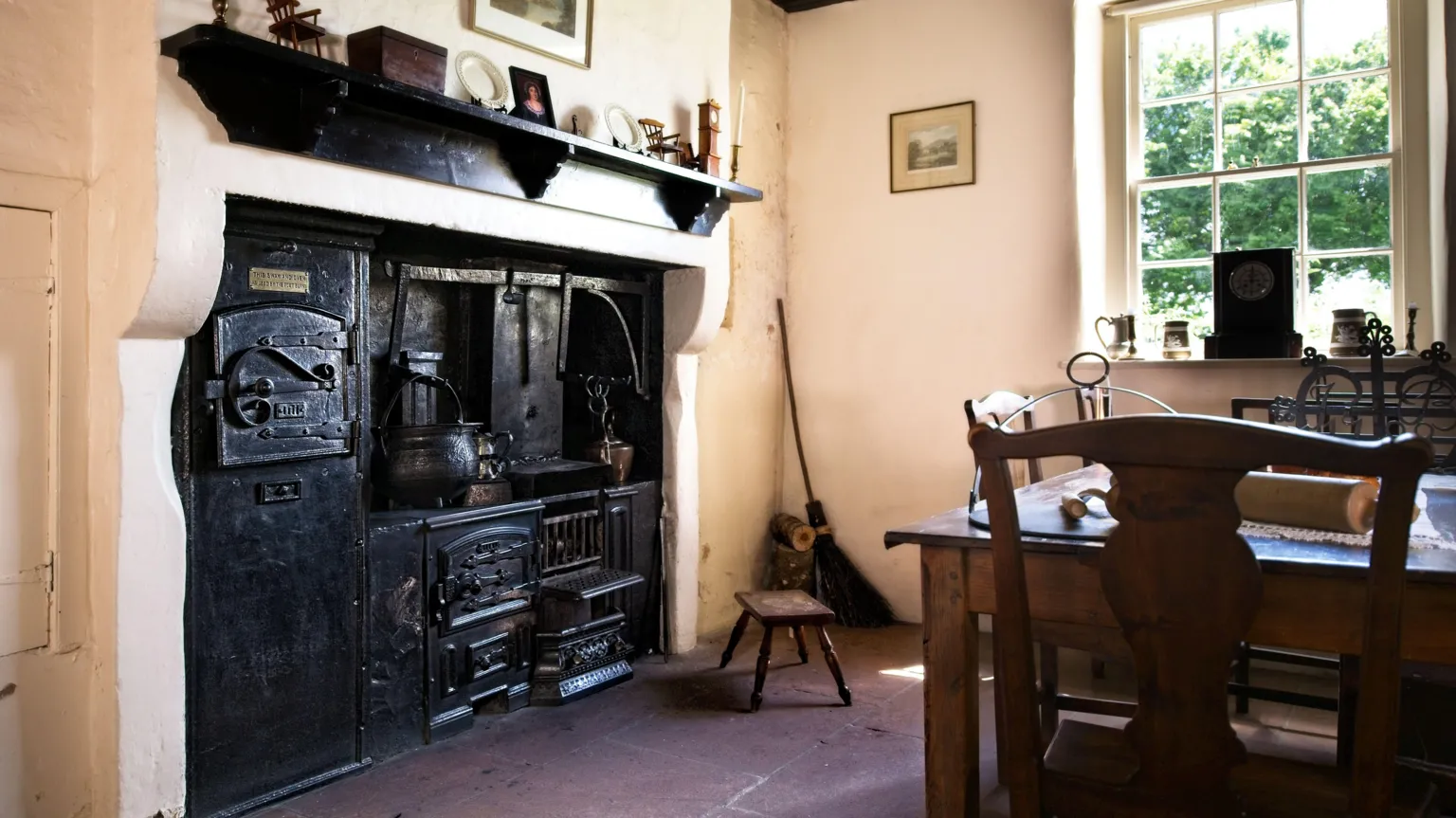 Ian Findlay An old iron stone built into the wall with a wooden shelf above it. A wooden table sits to the side underneath the window. The walls are painted cream.
