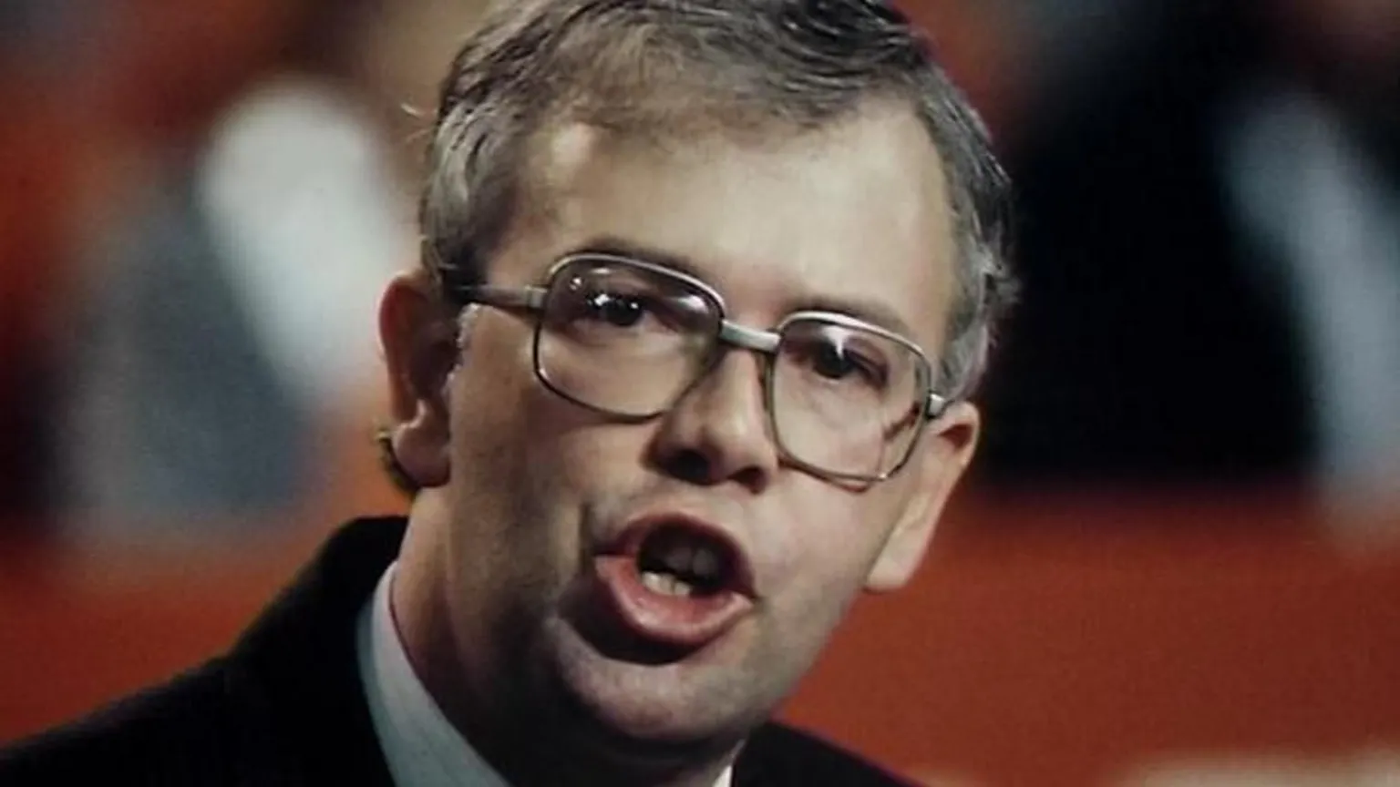 Old photo of Jim Wallace taken in the 1980s. He has dark grey hair and large glasses. HIs mouth is open mid speech. 