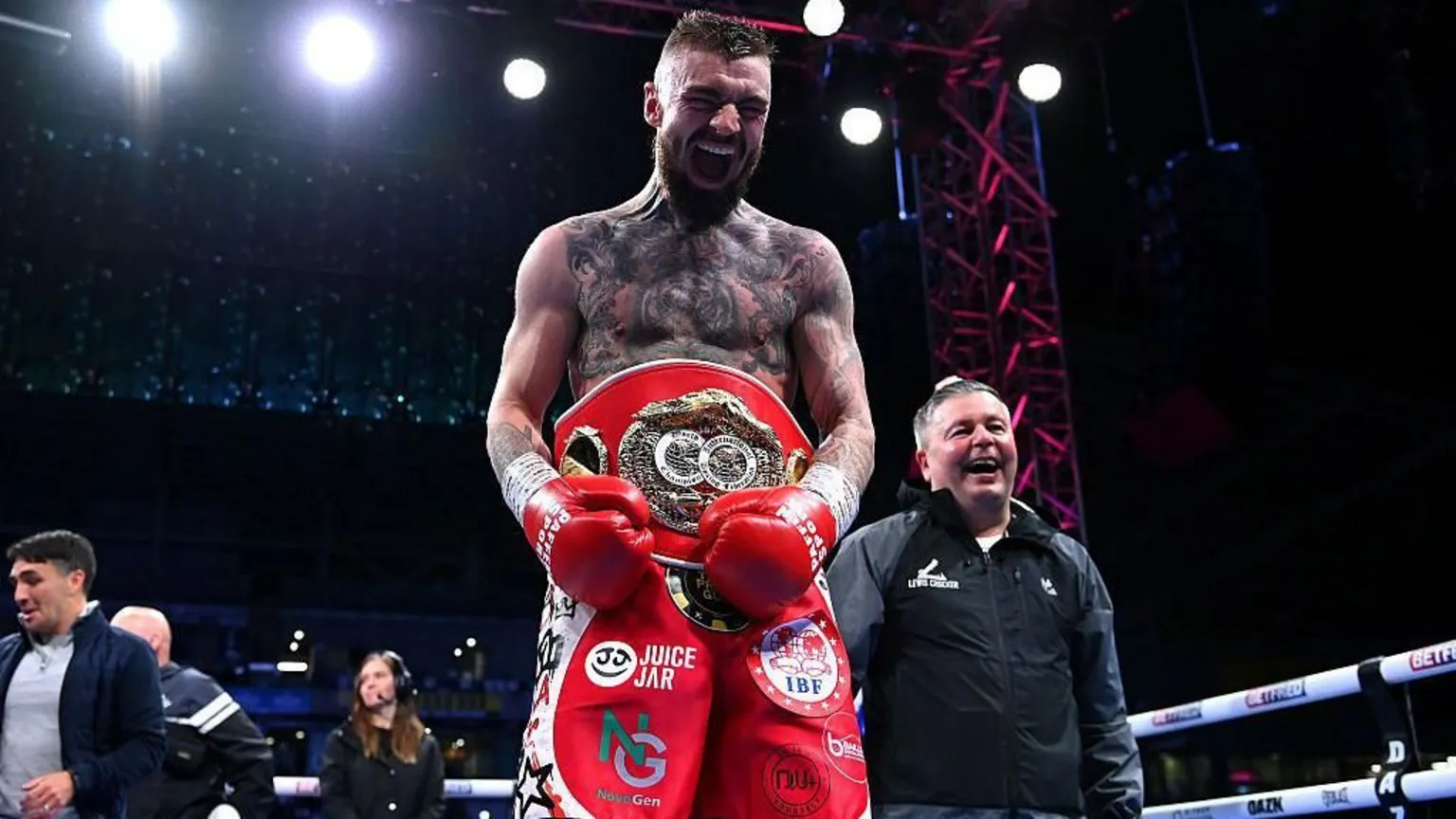  Lewis Crocker, a man with dark hair and a beard, tattoos on his chest, red shorts, wearing a red world title belt.