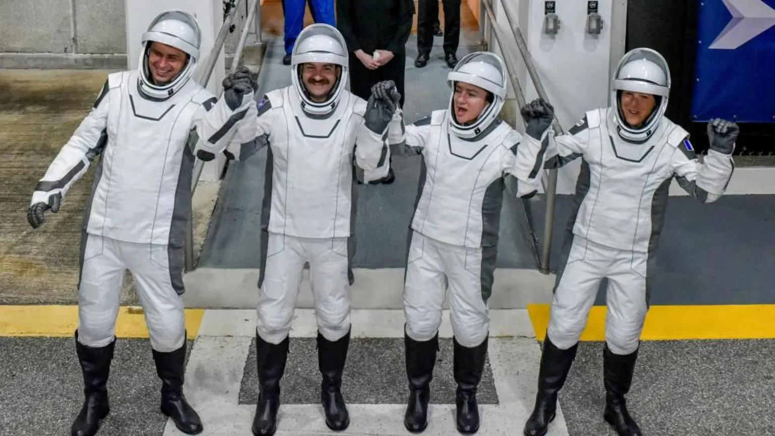  Four astronauts in white space suits hold hands and lift them in celebration at the Kenedy Space Centre entrance