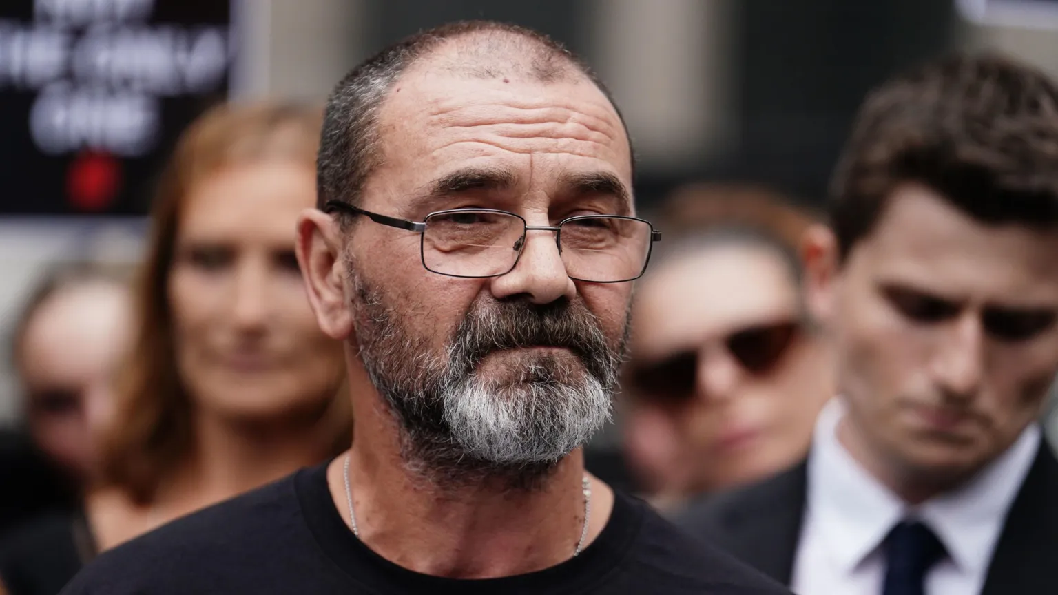  Andrew Malkinson wearing a black shirt standing outside next to a crowd.
