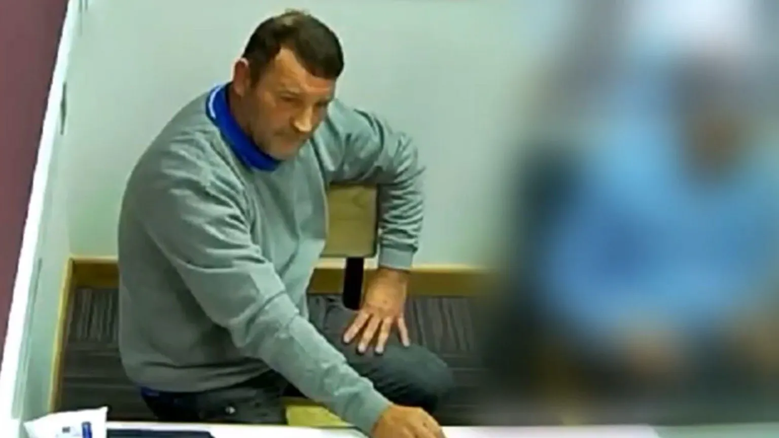 GMP Paul Quinn, sitting in a police interview room, has short dark hair and is wearing a grey sweatshirt over a blue top.