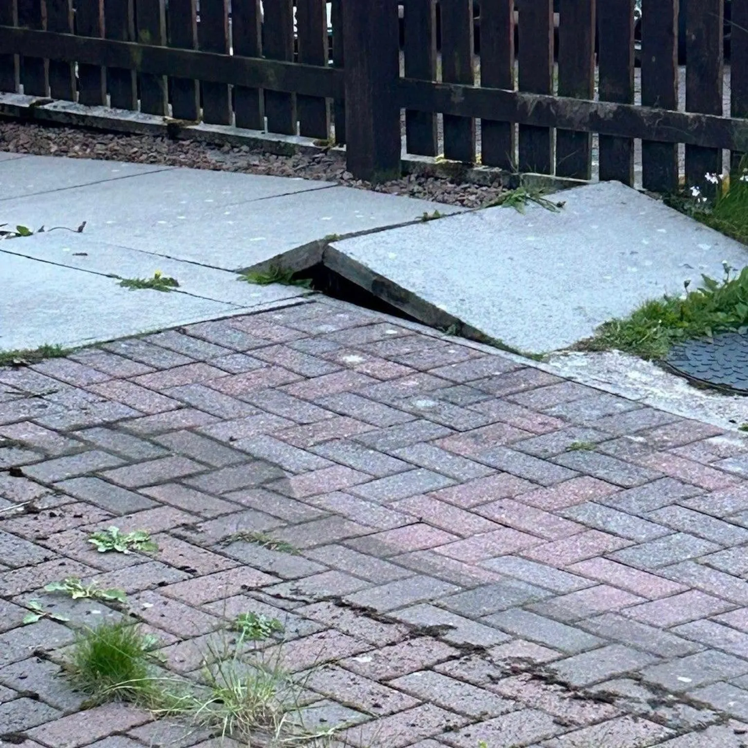 Simon Woodward A paving slab which has raised slightly with a fence in the background