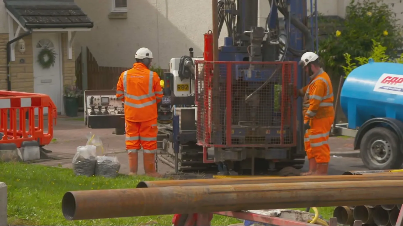 Two men in orange hi vis stand with drilling machinery in a residential street