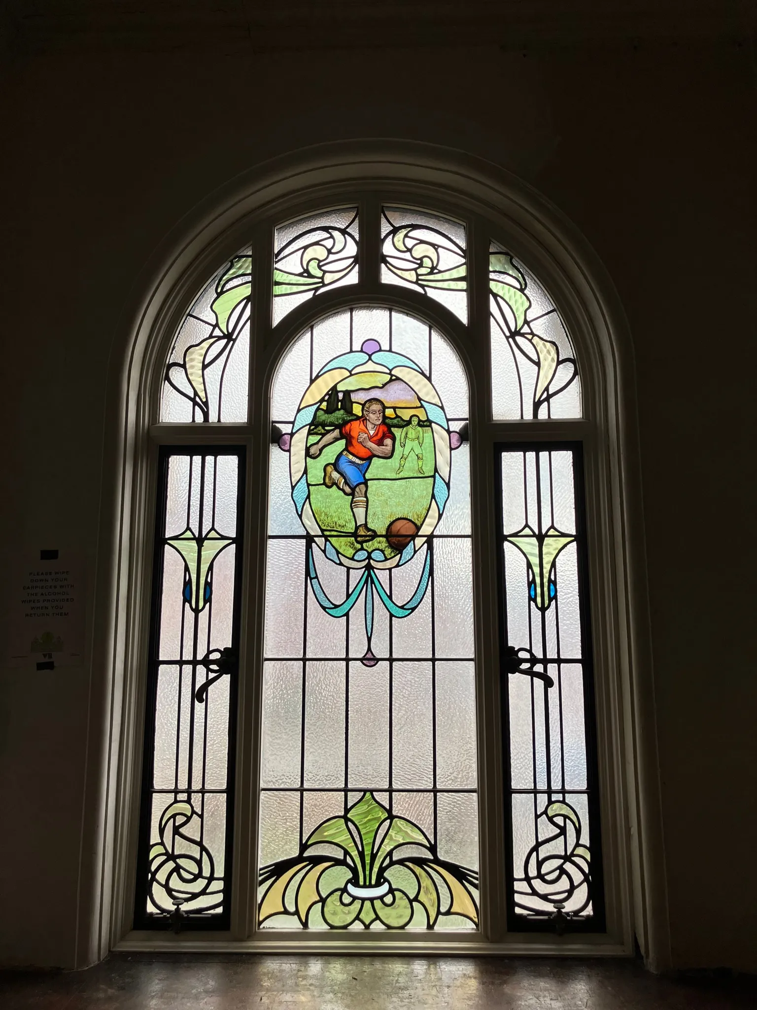 A close-up of a stained window with a middle panel showing a footballer about to kick a ball.
