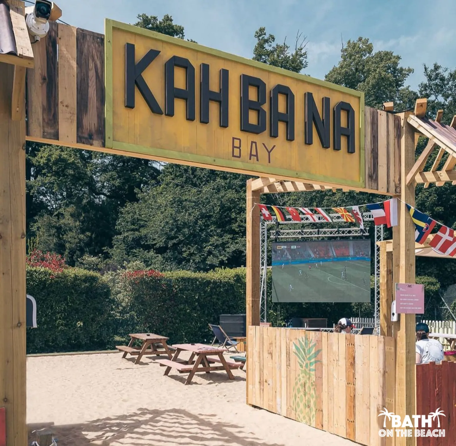 Bath on the Beach An outdoor beach-style bar with sand, benches and a screen showing the football