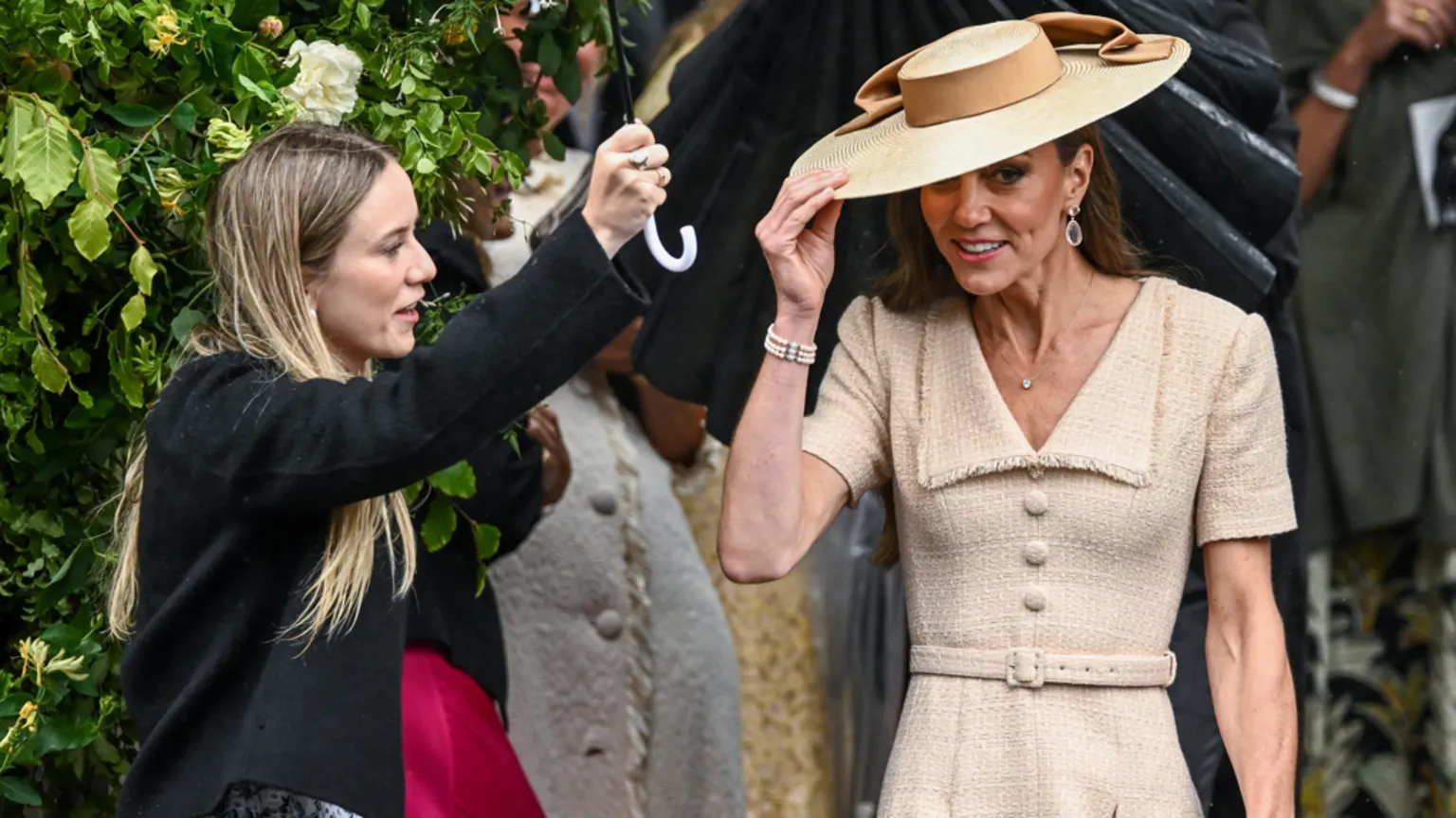  A woman is holding an umbrella above Kate Middleton.