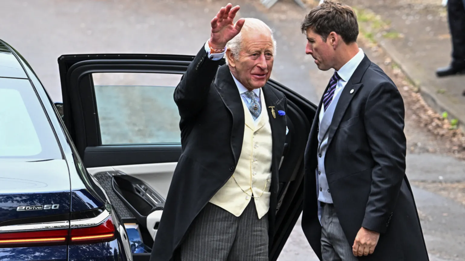  King Charles is waving to people after exiting a car through its door