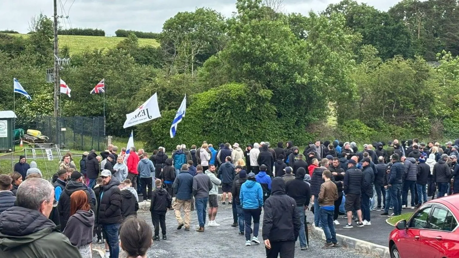 A crowd of around a hundred people can be seen in the foreground standing around ahead of the arrival of a Palestine solidarity march which is due to pass through the village