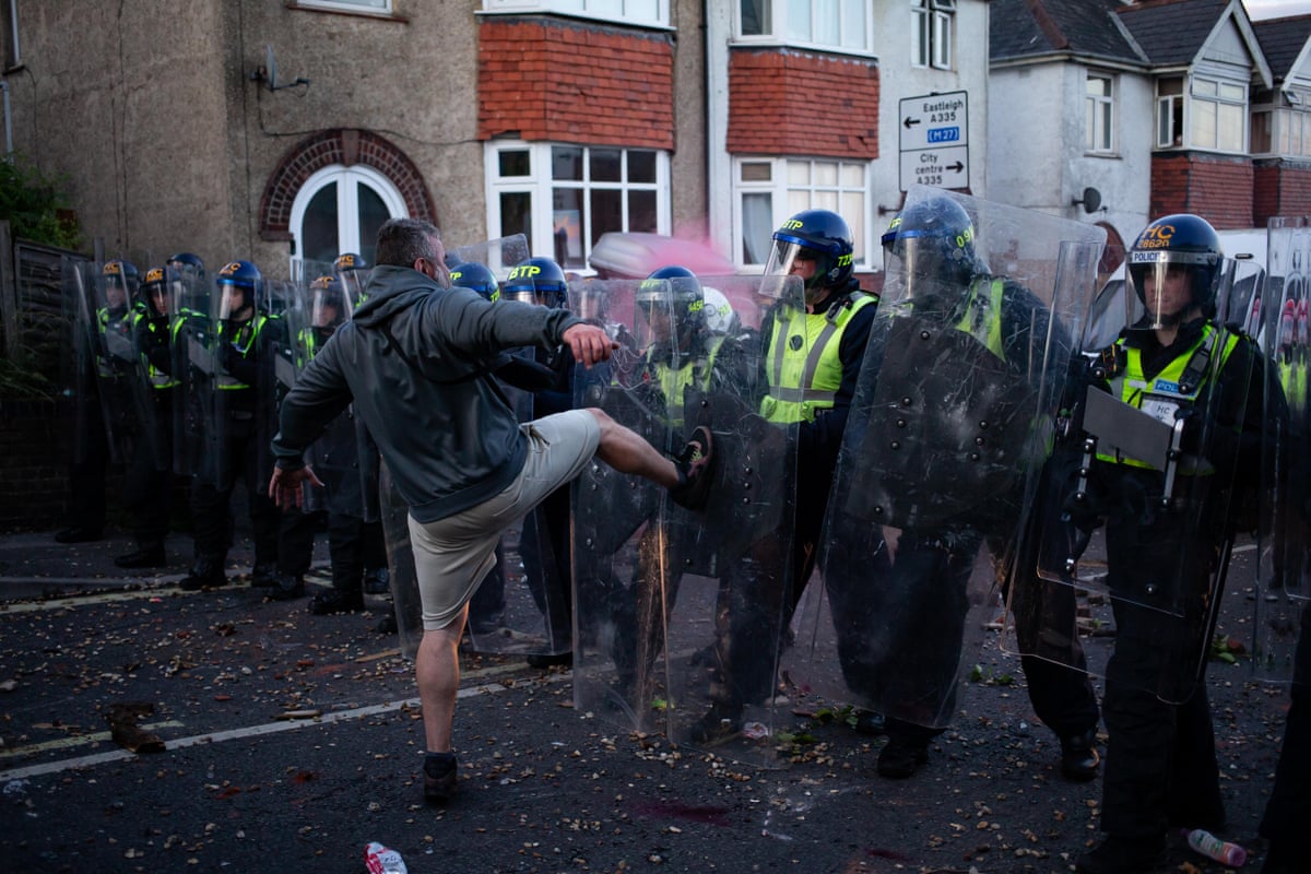 A man kicks out at line of police officers using riot shields