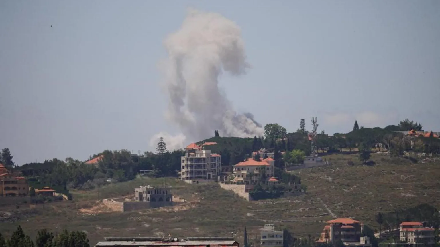 Smoke rising after a strike in southern Lebanon - several buildings are visible on the hillside