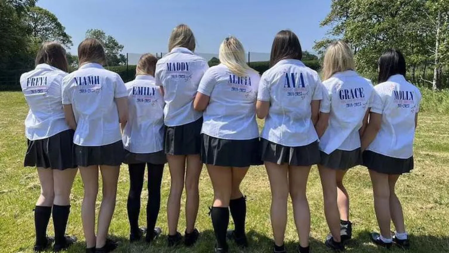 FromMe2uu A group of girls are standing with their school shirts in a field. They have personalised names on the back of the shirts.