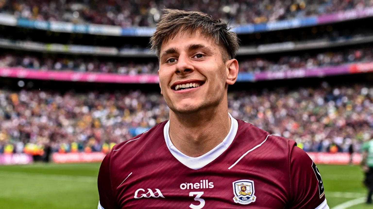 Seán Fitzgerald is standing in a pitch in the middle of a huge stadium. He's wearing a maroon GAA jersey. The stadium is full of people.