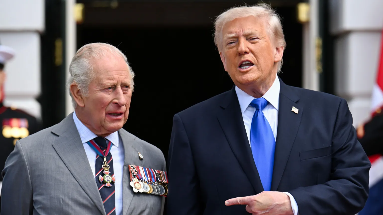  King Charles and President Donald Trump standing outside, with Trump pointing a finger at Charles. 