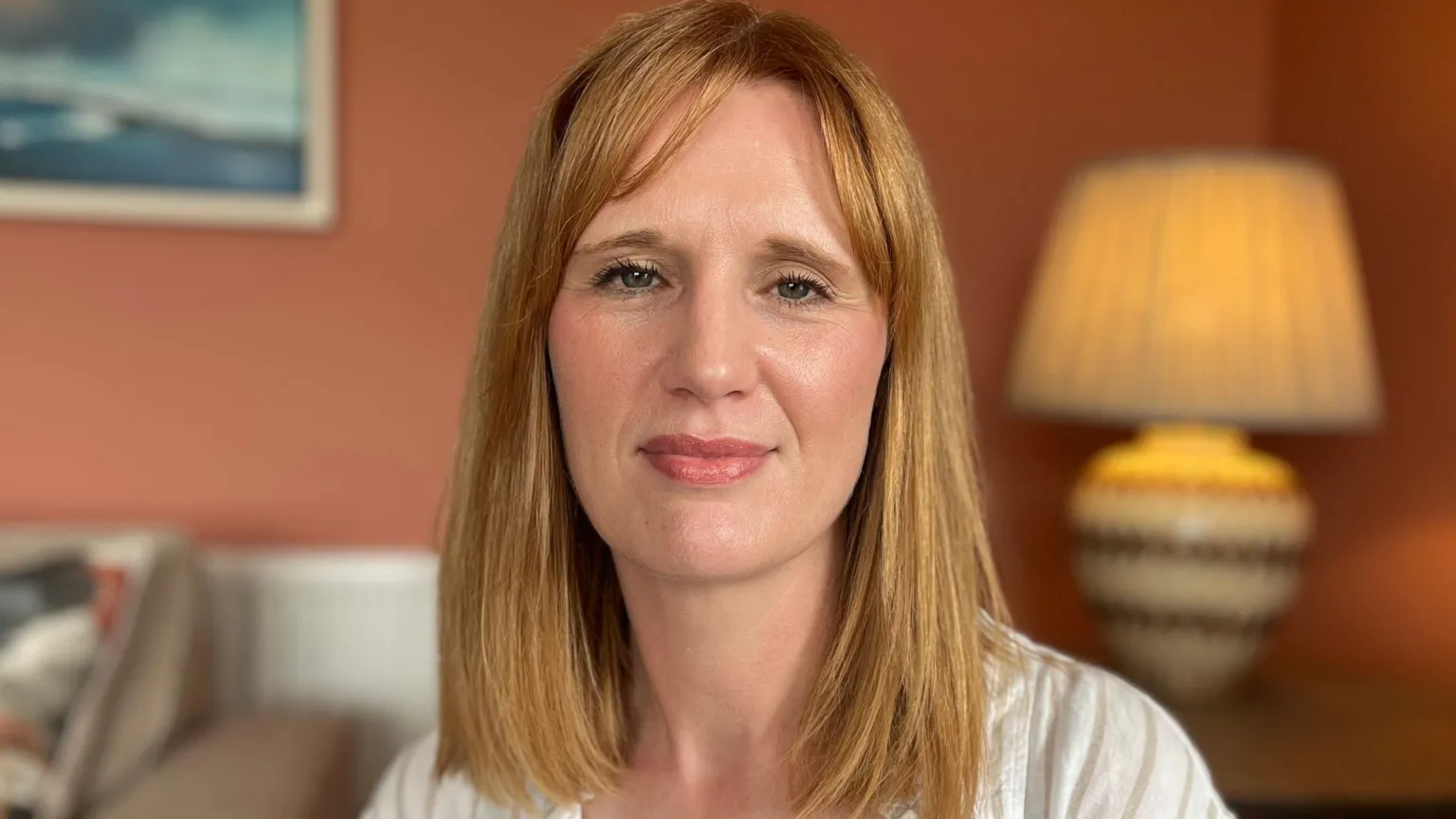 A woman with red hair looking at the camera, she has a white shirt