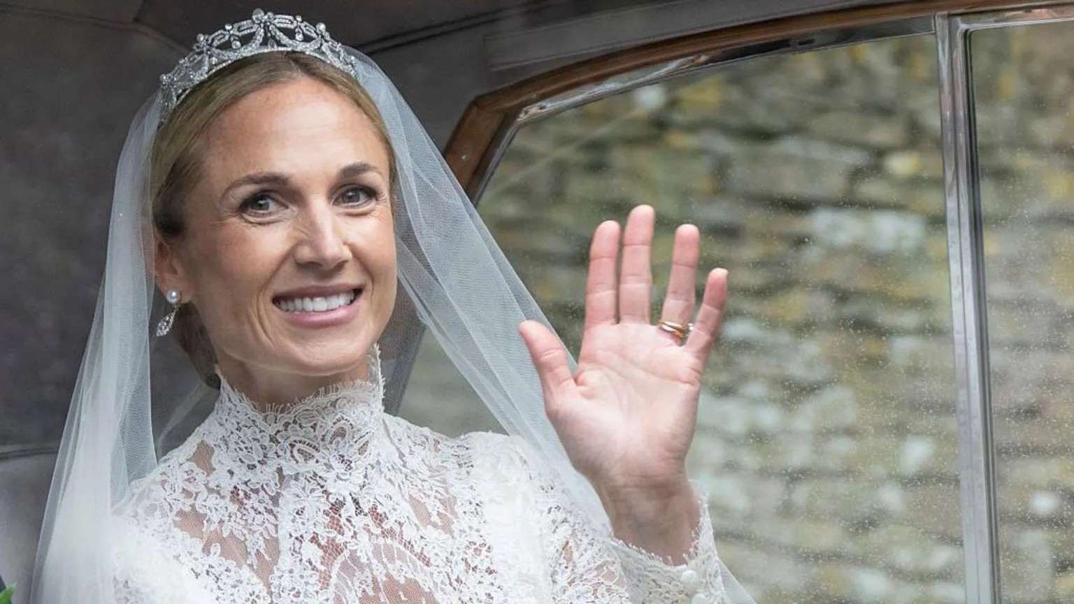 Mark Cuthbert/UK Press via Harriet Sperling waves in a white wedding dress and tiara from a car