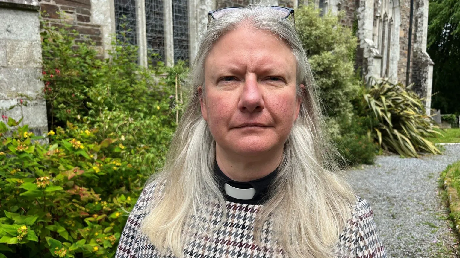 Reverend Claire Reynolds stood outside All Saints Church in Okehampton on Sunday afternoon. She has grey hair and has glasses on her head.