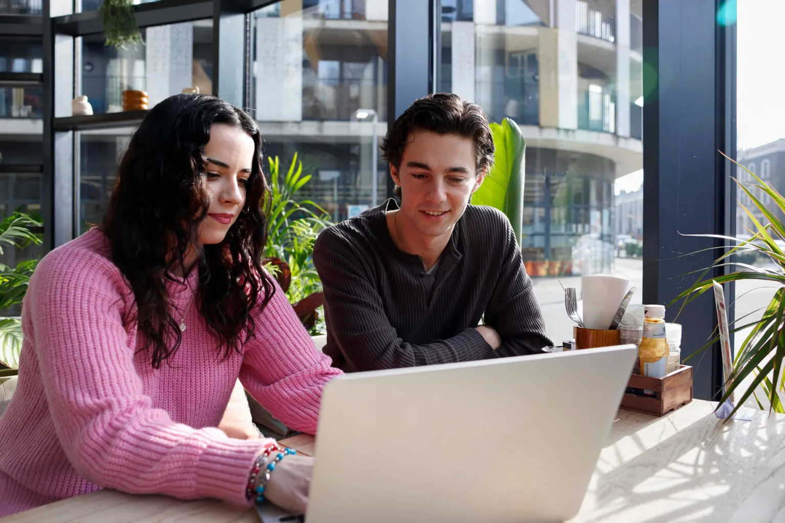 A young woman and a man looking at a laptop screen in a cafe.