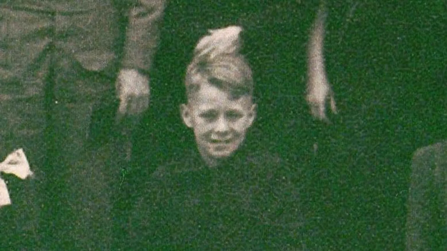 BBC/Minnow Films/Ted Bush A young boy with fair hair, wearing dark clothing, smiles at the camera. The image is in black and white