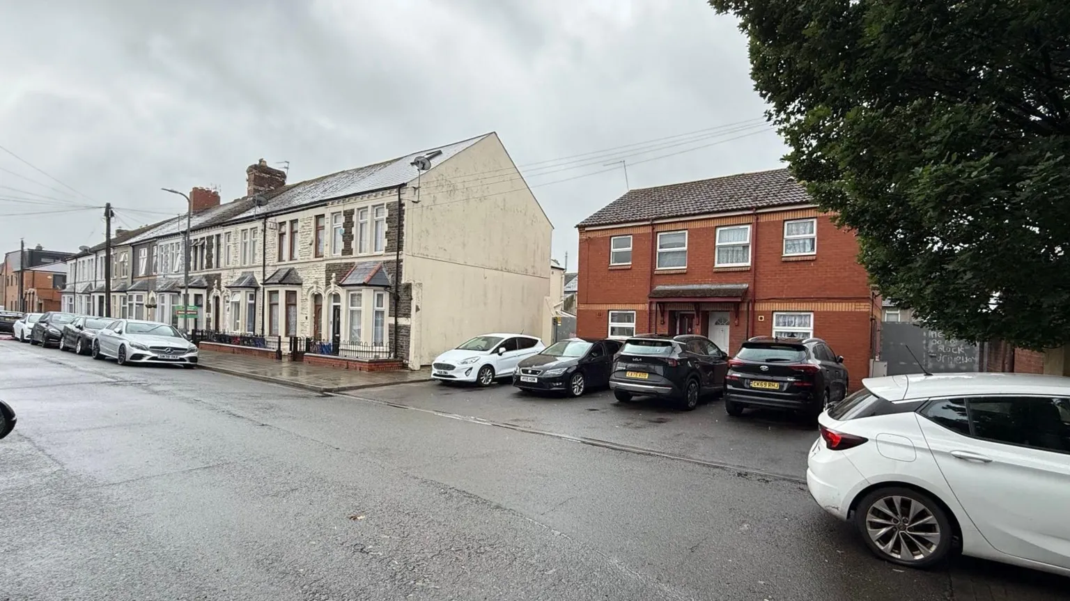 A long row of traditional stone and brick victorian terraced houses lines the left side of the street, featuring bay windows and small front gated areas. The other half of the street is modern built homes constructed from red brick and uPVC window frames.