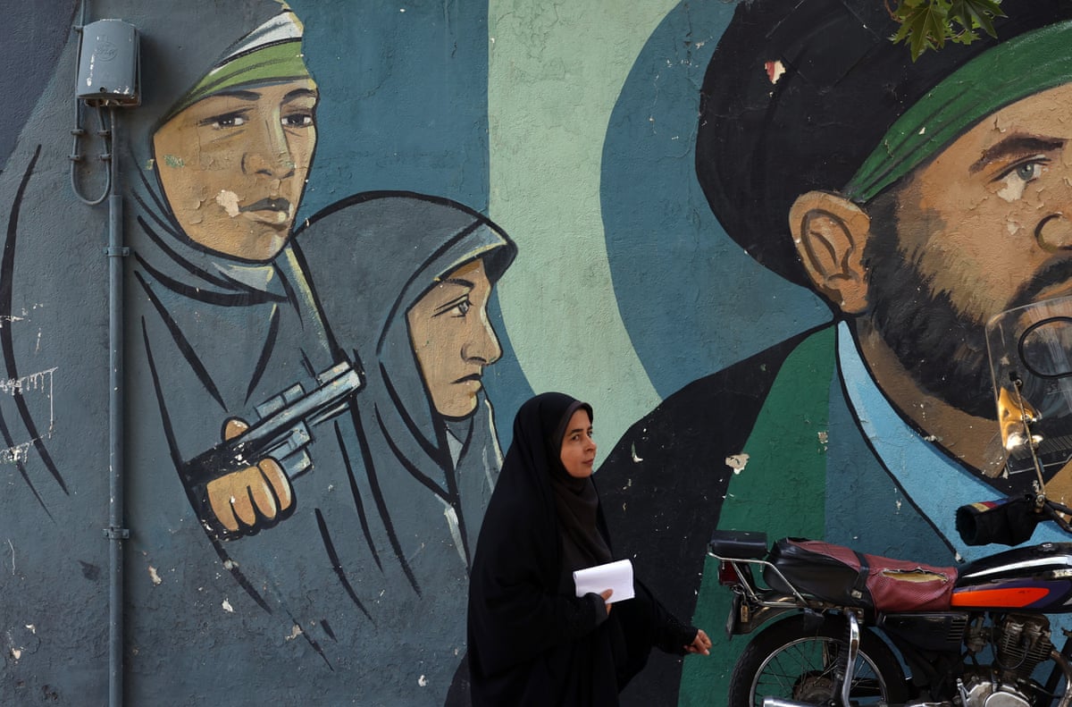 An Iranian woman walks past a wall painting of Iranian women soldiers on a street in Tehran.